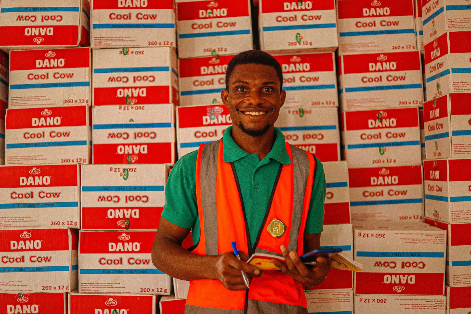 A field worker holding a phone in front of stacked cartons